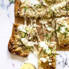 A pizza with ranch sauce, zucchini, garlic, chicken, onions, and dill toppings.