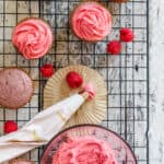 Pink cupcakes with fresh raspberries around and a piping bag of raspberry frosting.