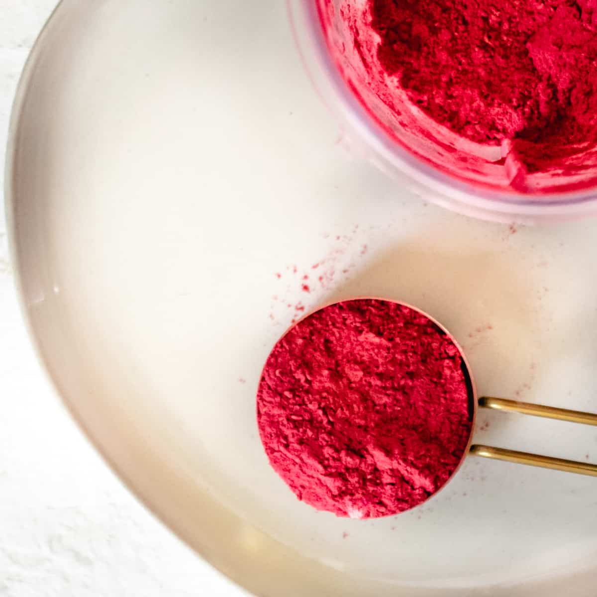 Magenta colored fruit powder in a brass measuring cup.