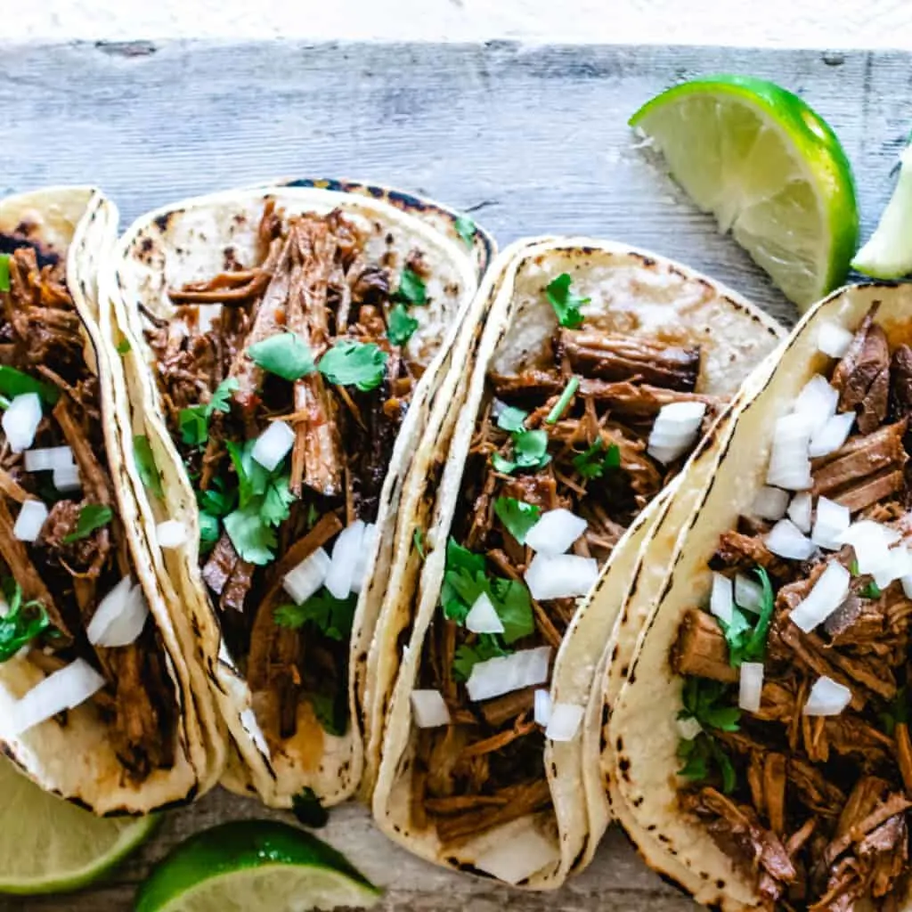 beef barbacoa in corn tortillas with cilantro, onion, and fresh lime