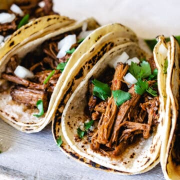 tacos de barbacoa served with corn tortillas and lime wedges