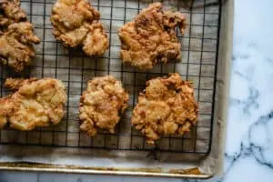 fried chicken patties draining on a baking rack, over a parchment paper lined baking sheet.