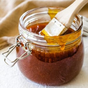 glass jar with basting brush and apricot barbecue sauce on white textured surface