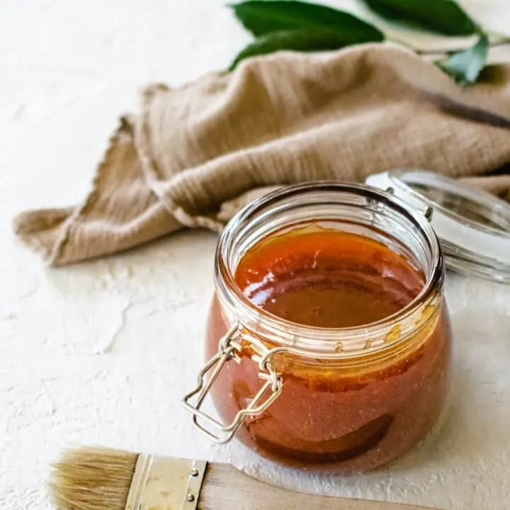 glass hinged jar of apricot barbecue sauce with basting brush next to taupe flour sack cloth on white stone surface