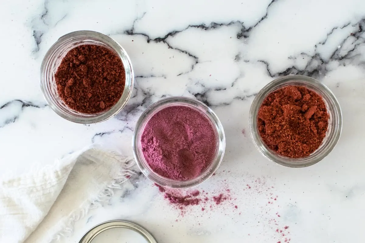 3 small jars of various shades of homemade fruit powders on marble counter top