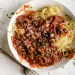 spaghetti with meat sauce, basil ribbons, Parmesan cheese and a fork in a white bowl on white stone counter top