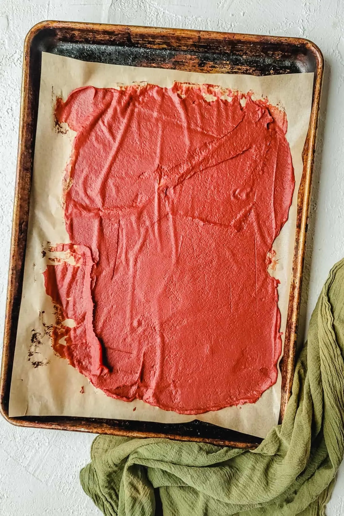 A baking sheet with tomato paste spread over it.