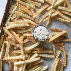 fried, wavy cut potato sticks on baking sheet with a silver cup of fry sauce