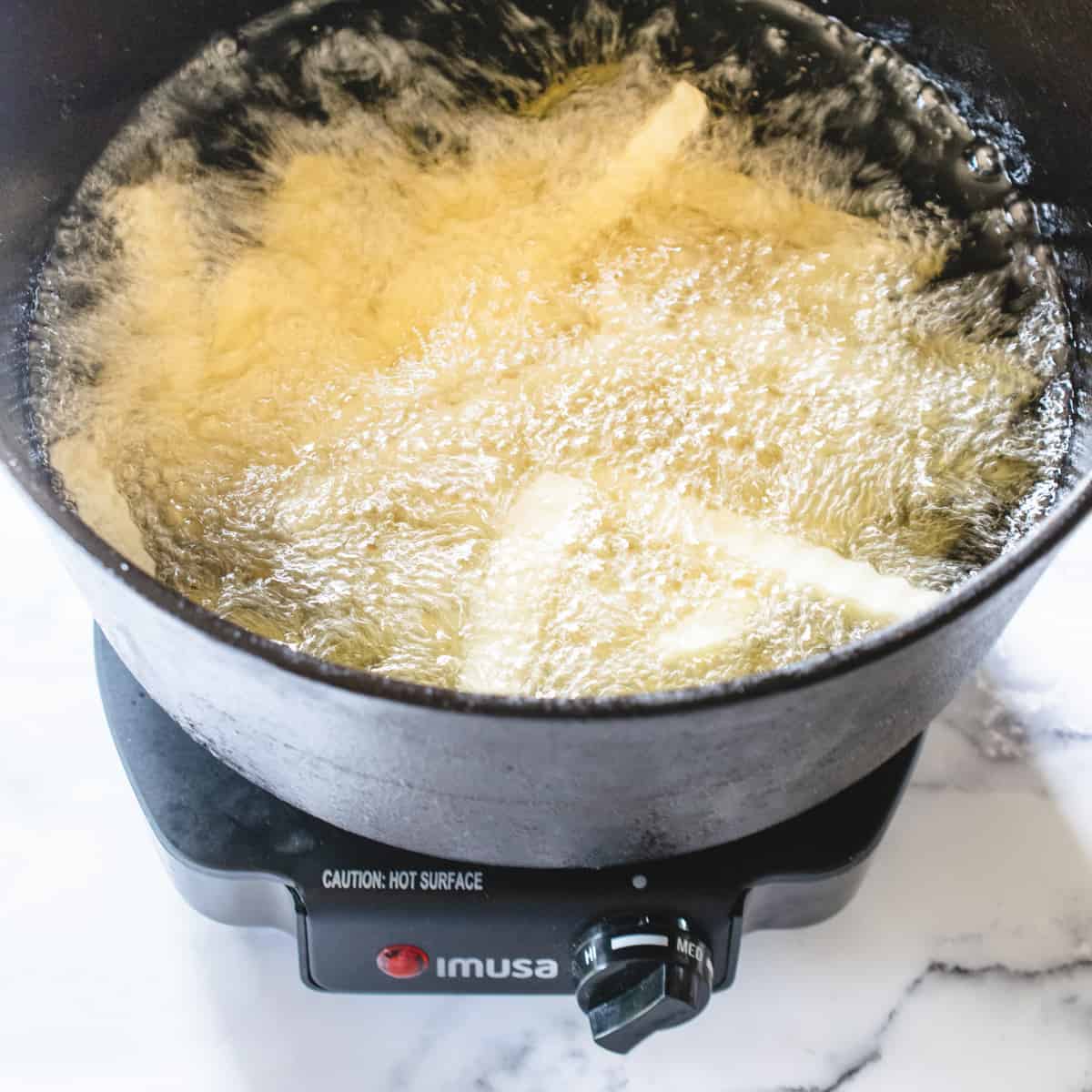 French fries being deep fried in a pot in boiling oil.