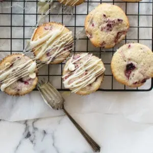 muffins drizzled with white chocolate on a cooling rack next to a fork