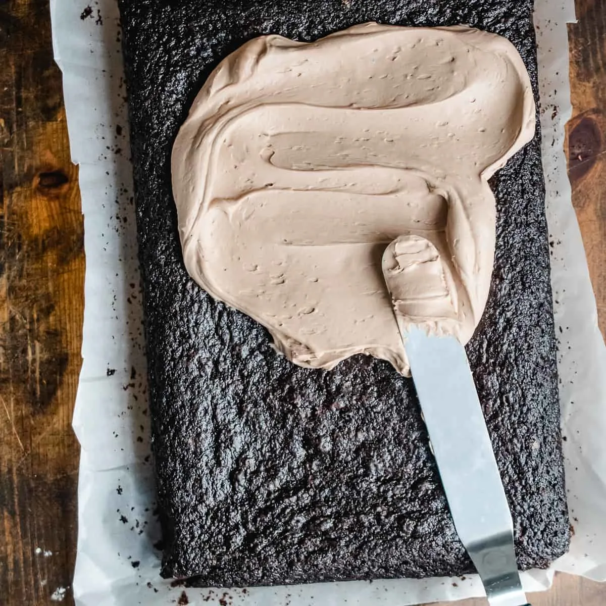 Chocolate frosting being spread on a chocolate sheet cake. 