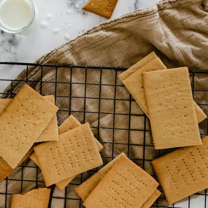 graham crackers on wire rack over taupe cloth with glass of milk and crumbs