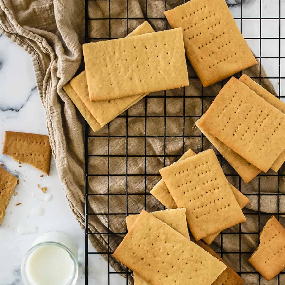 Graham crackers on a baking rack next to a glass of milk.