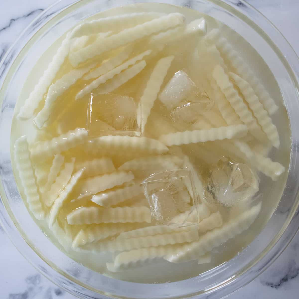 Crinkle cut French fries in a bowl of ice water
