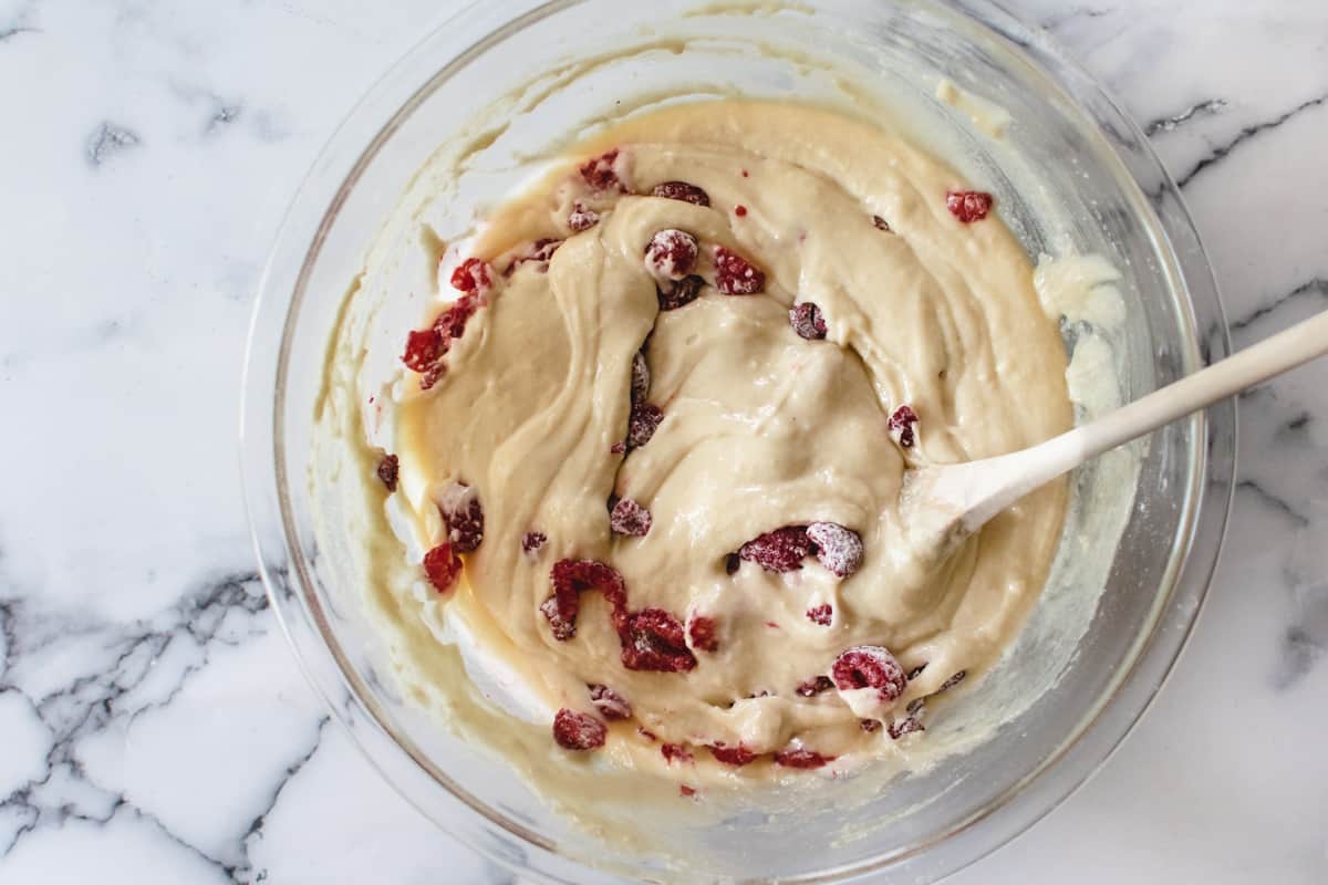 glass bowl with raspberry muffin batter and wooden spoon on marble background