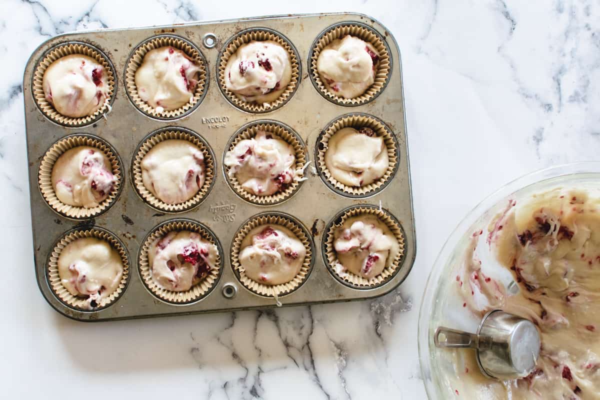 muffin tin filled with batter next to mixing bowl and spoon