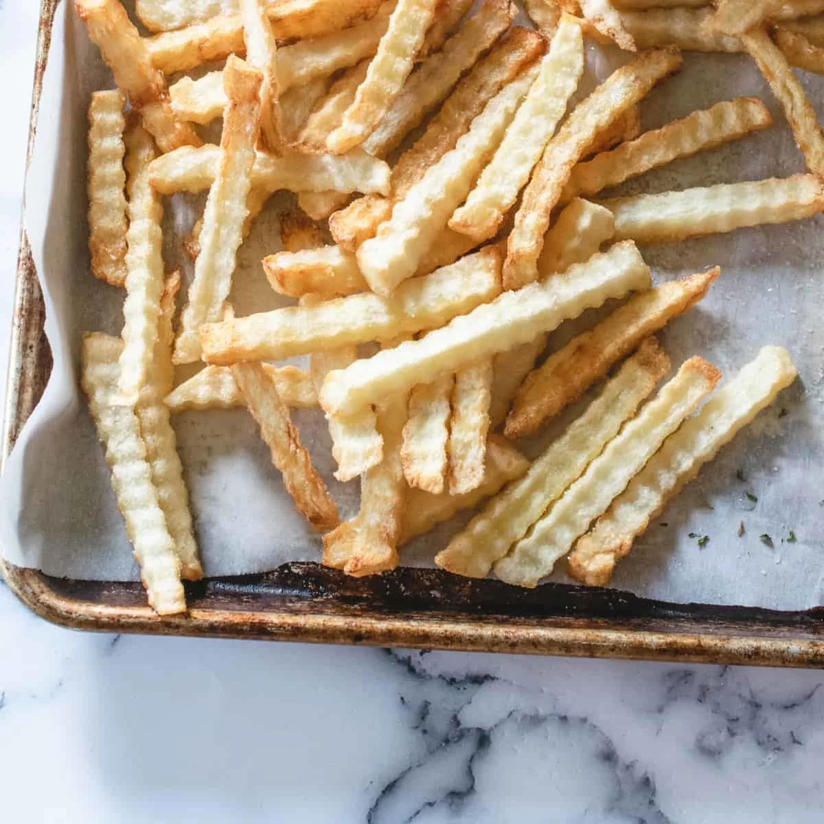 Crinkle cut fries on a baking sheet with salt.