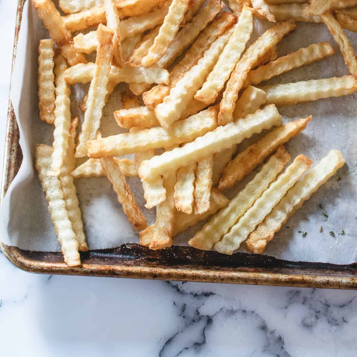 deep fried wavy cut potatoes arranged in a single layer on a parchment paper lined baking sheet