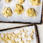 Nests of homemade pasta ribbons and homemade bowtie pasta shapes on baking sheets.
