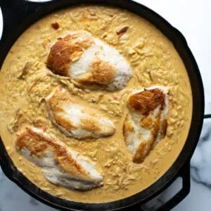 A skillet with chicken breast and orzo in a creamy sauce.