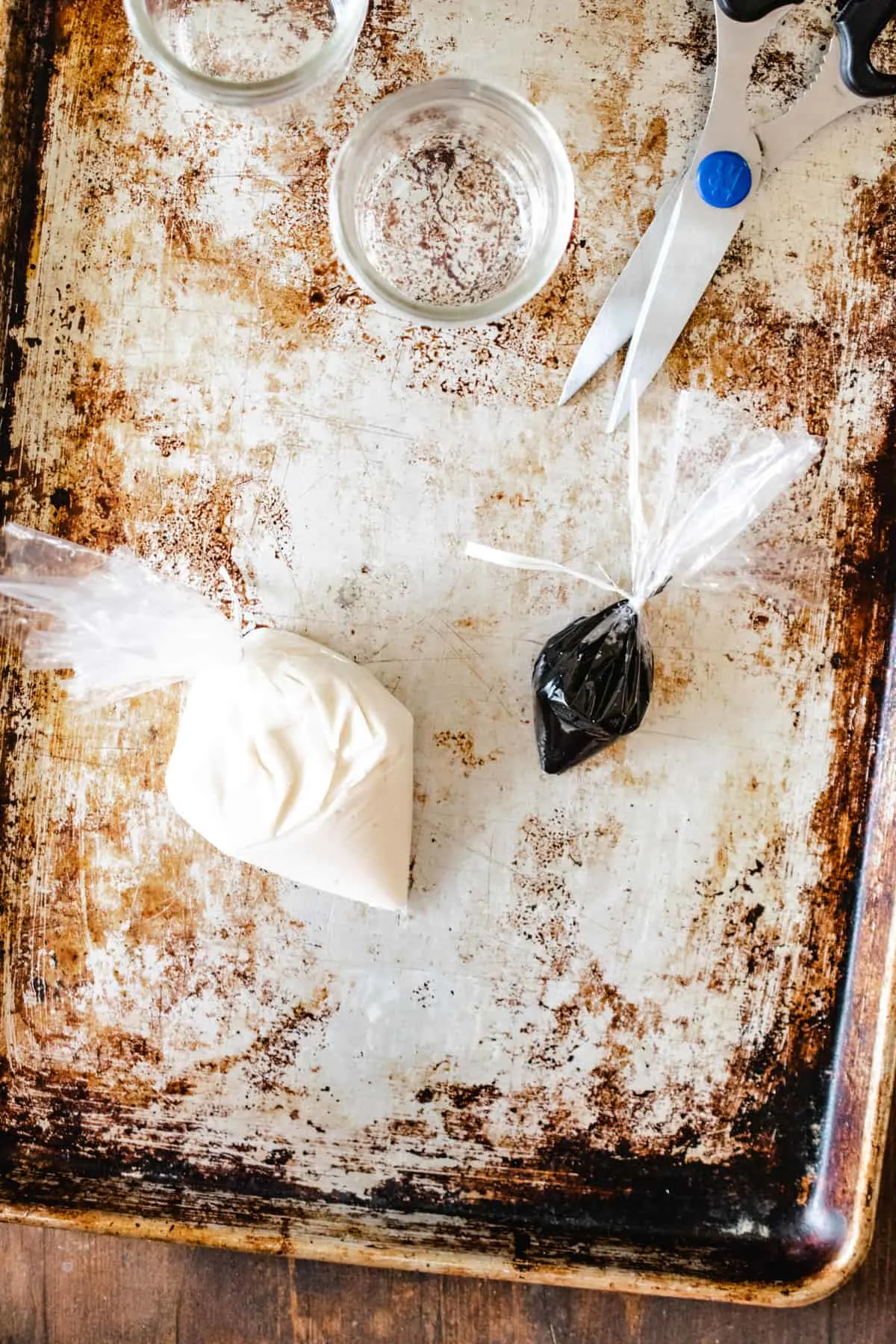 White icing in a plastic bag, next to small bag of black icing by a pair of scissors. 