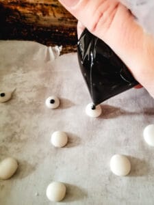 Black dots being piped onto larger white dots with a bag of frosting.