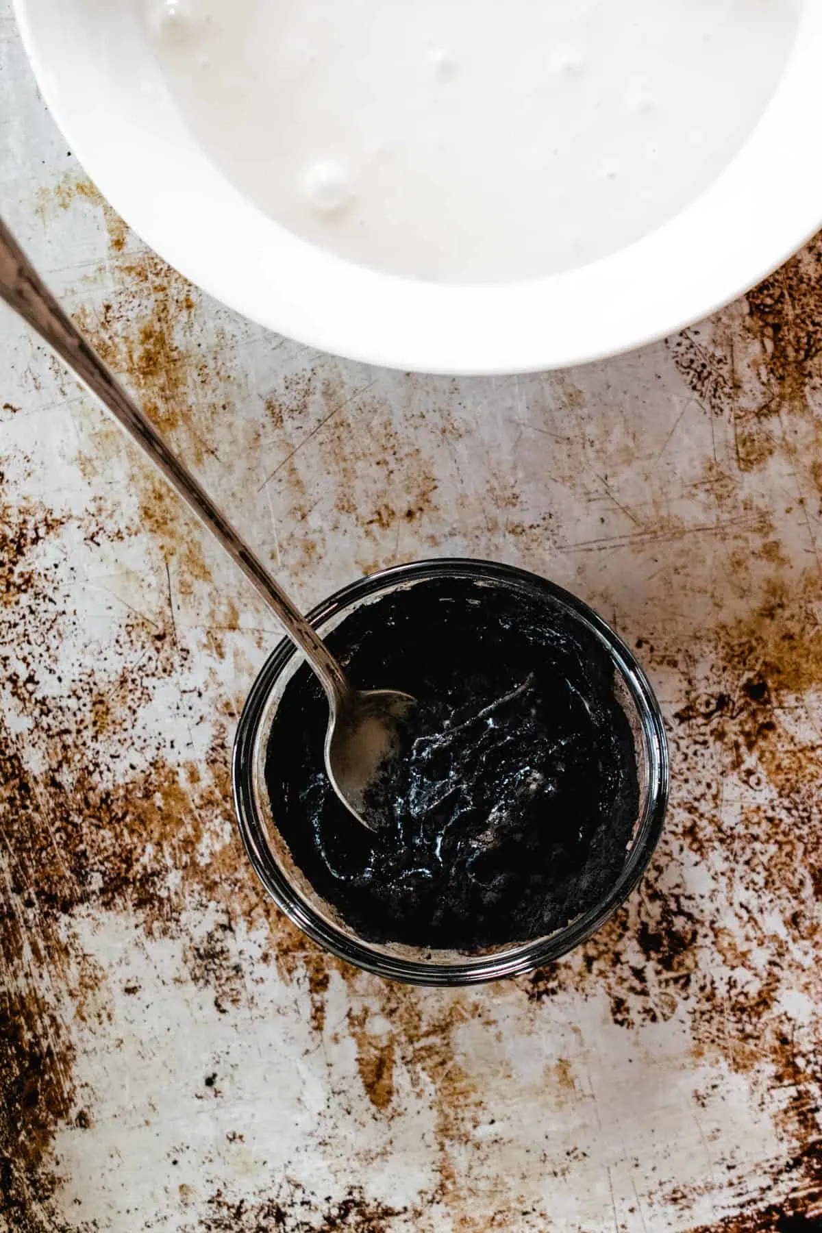 Black icing like confection in a small glass bowl next to a larger white bowl with white icing. 