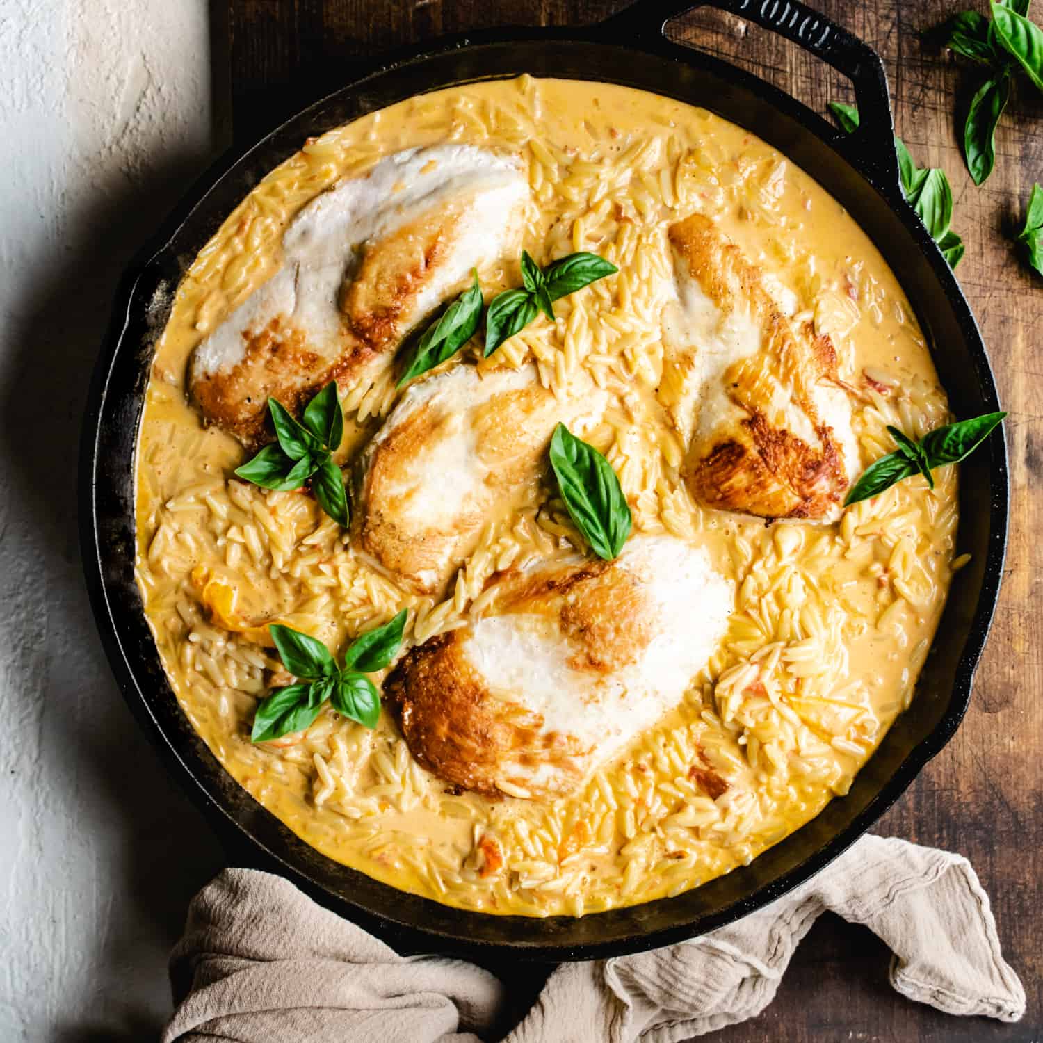Cast iron skillet with taupe towel filled with orzo in a yellow, creamy sauce, topped with chicken breast.
