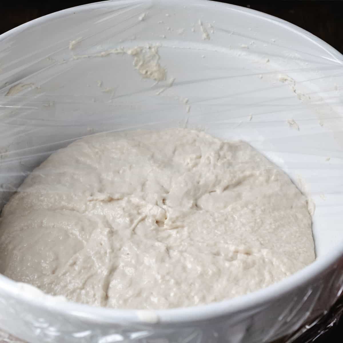 Bread dough in a bowl, covered with plastic wrap.