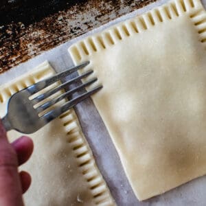 Homemade pop tarts being pressed with the tines of a fork to seal.