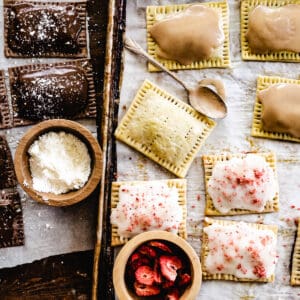 Chocolate, strawberry and cinnamon and brown sugar homemade pop tarts on baking sheet with toppings and a spoon.