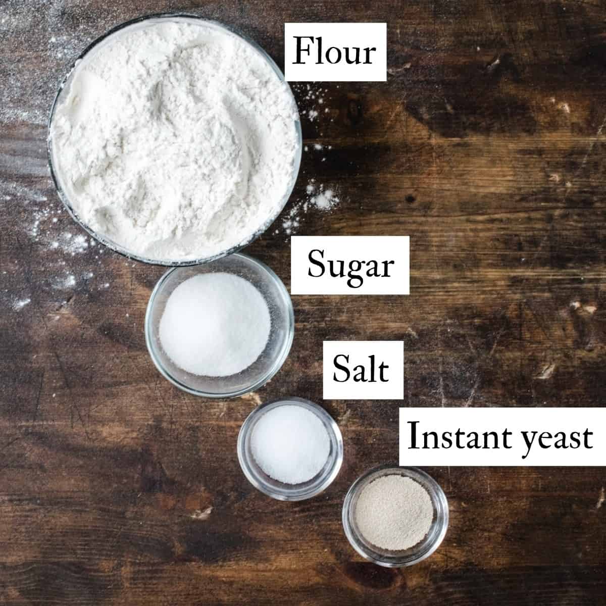 Bowls of flour, sugar, salt and yeast with text labels.