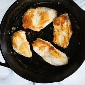 Chicken breasts searing in a cast iron pan.