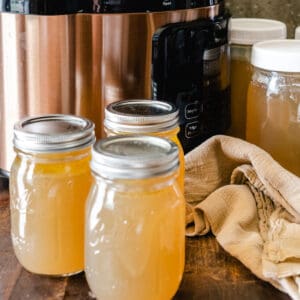 Electric pressure cooker behind mason jars full of bone broth.