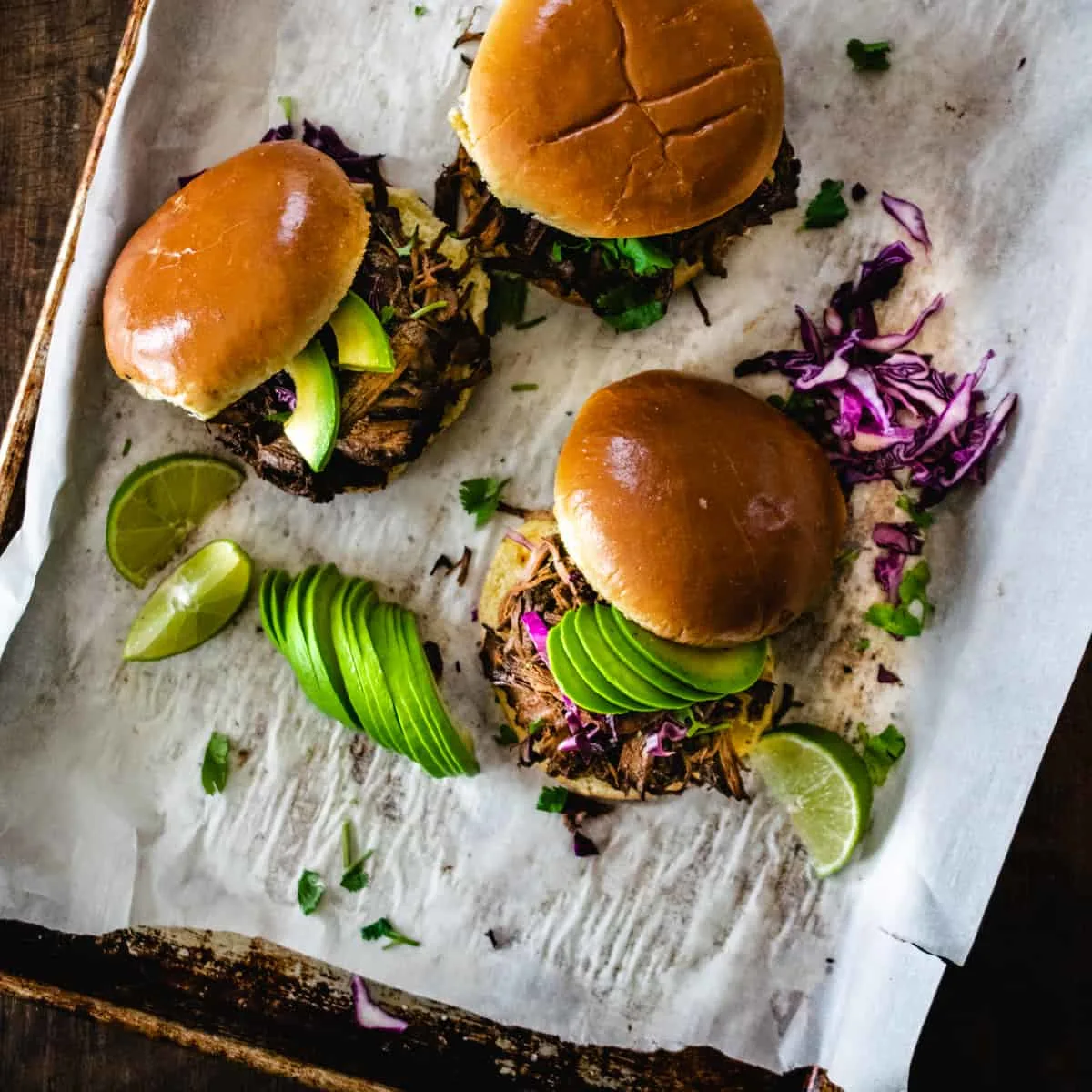 Three shredded beef sandwiches topped with avocado and lime.