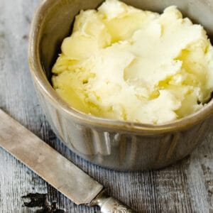 Beige ramekin full of butter next to rustic butter knife.