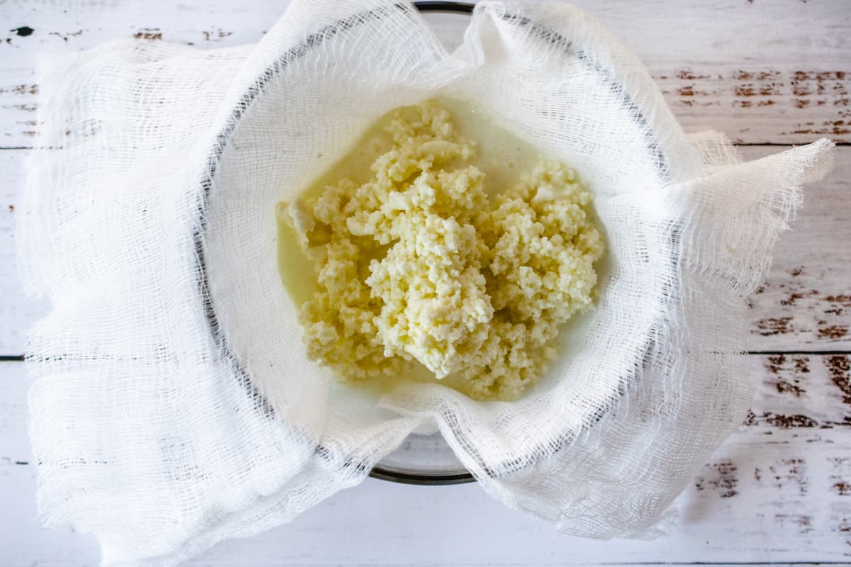Butter solids in a piece of cheesecloth being strained over a glass bowl. 