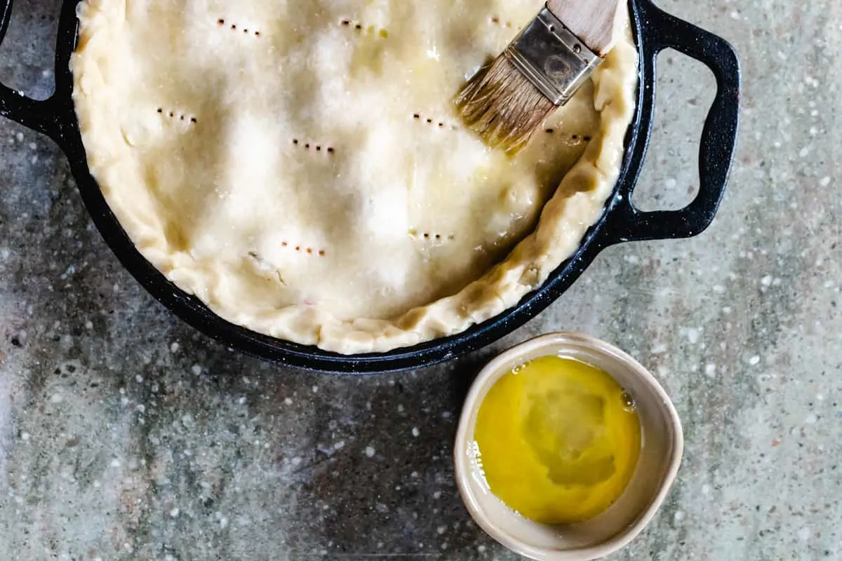 Pastry brush brushing pie crust with a beaten egg before baking.