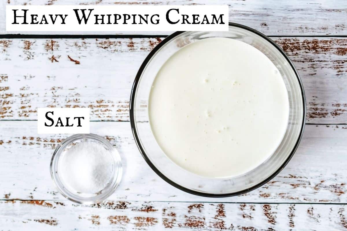 A bowl of heavy cream next to a small bowl of salt on distressed wooden backdrop.