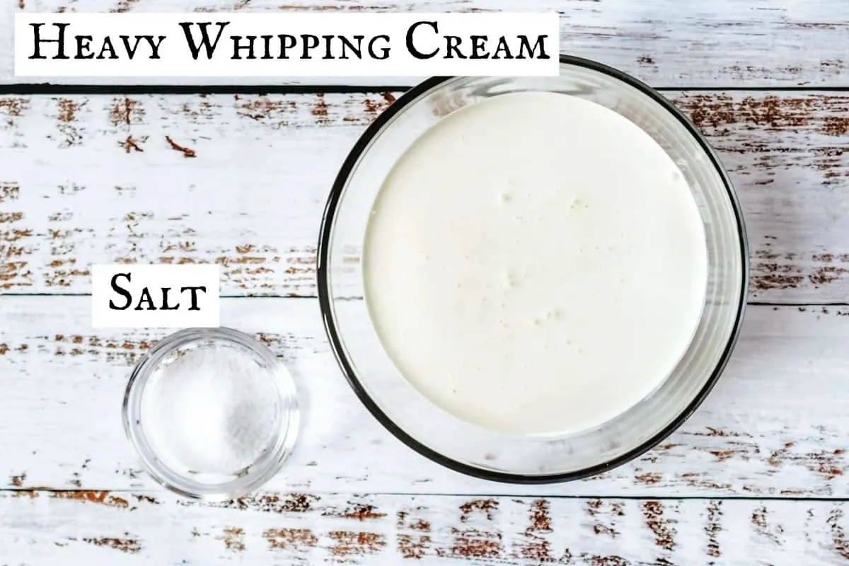 A bowl of heavy cream next to a small bowl of salt on distressed wooden backdrop.