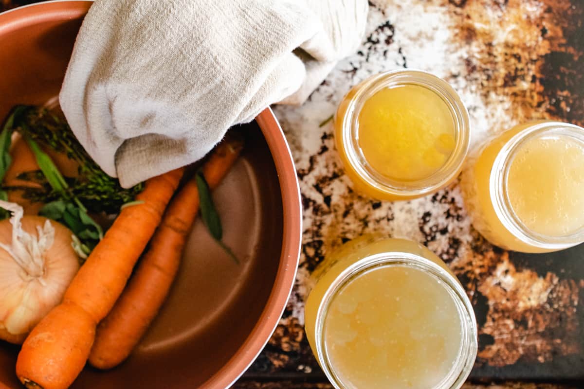 Pot with vegetable scraps next to open jars of broth.