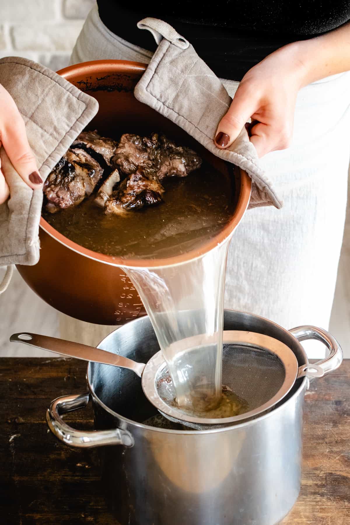 Pouring beef bone broth through a mesh strainer. 