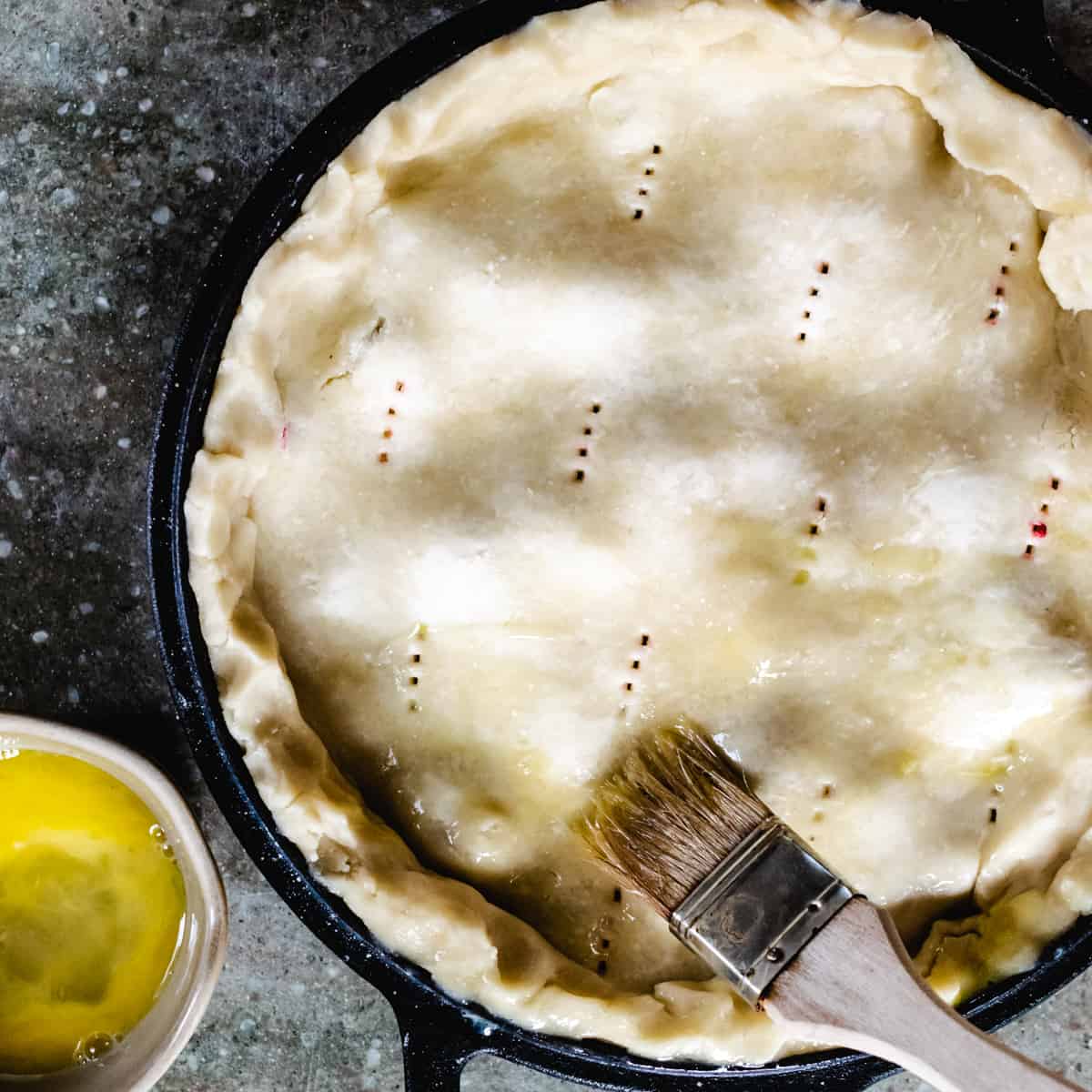 Uncooked pie being brushed with a beaten egg.