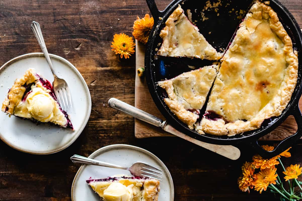 Slices of triple berry pie on plates with scoops of vanilla ice cream. 