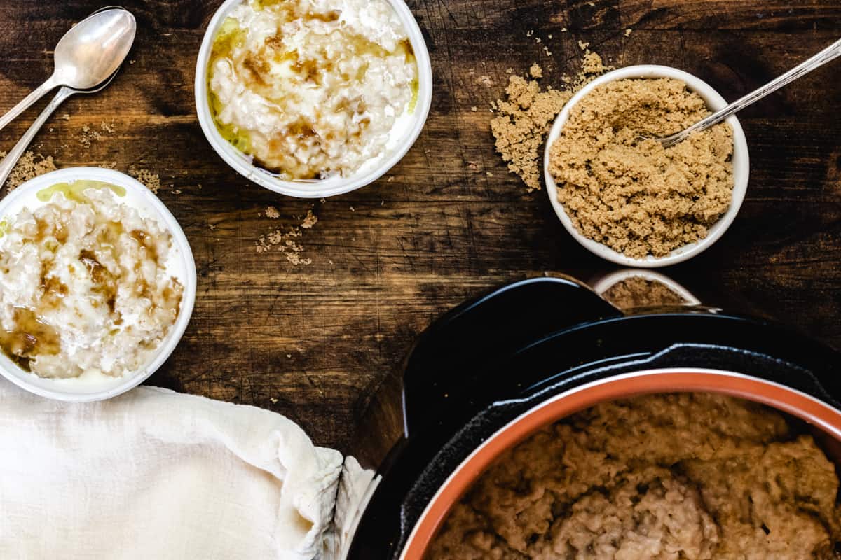 Two bowls of oatmeal next to a pressure cooker filled with fresh cooked oatmeal.