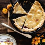Pie with two slices cut out surrounded by orange flowers on wooden cutting board.
