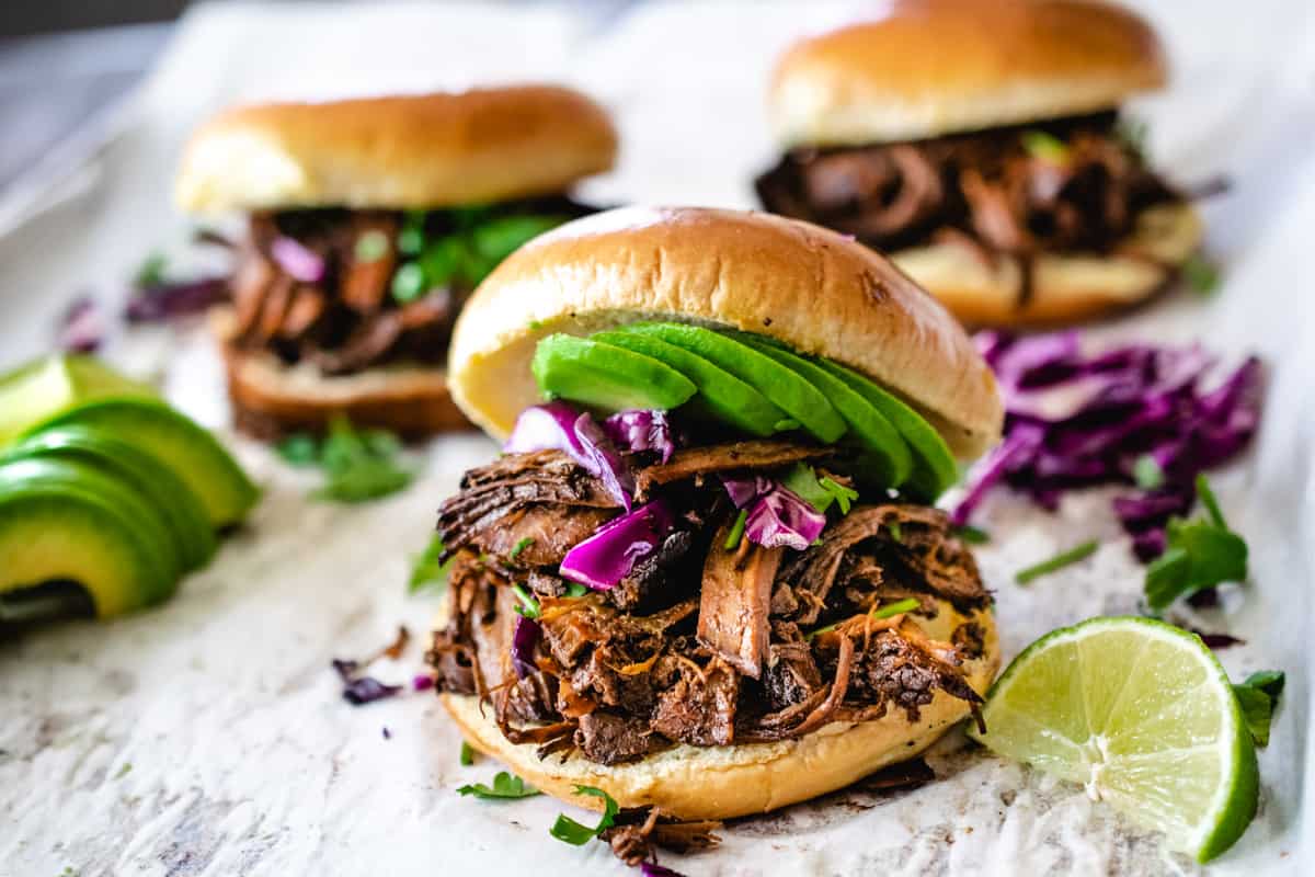 Shredded beef on a hamburger bun with avocado, lime, cilantro and cabbage.