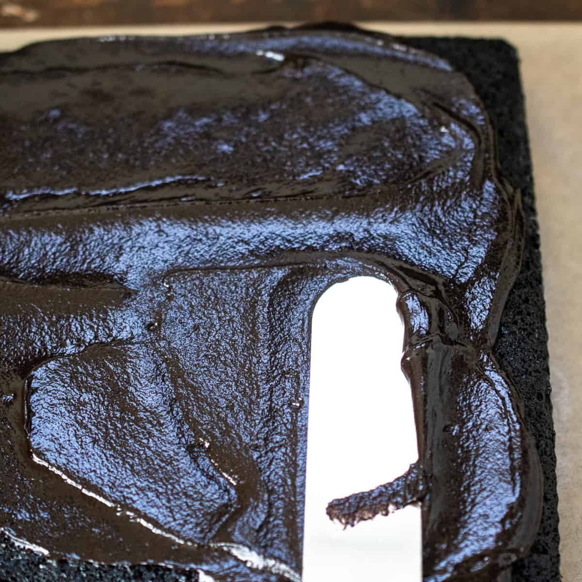 Chocolate ganache icing being spread over a cake with an offset spatula.
