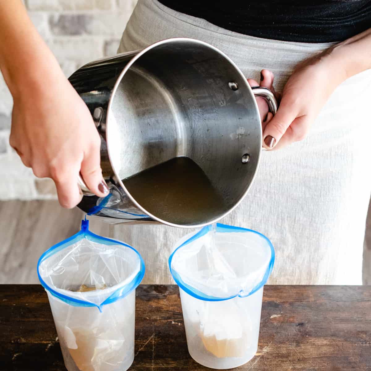 Person pouring stock out of a pot into plastic zip lock bags.