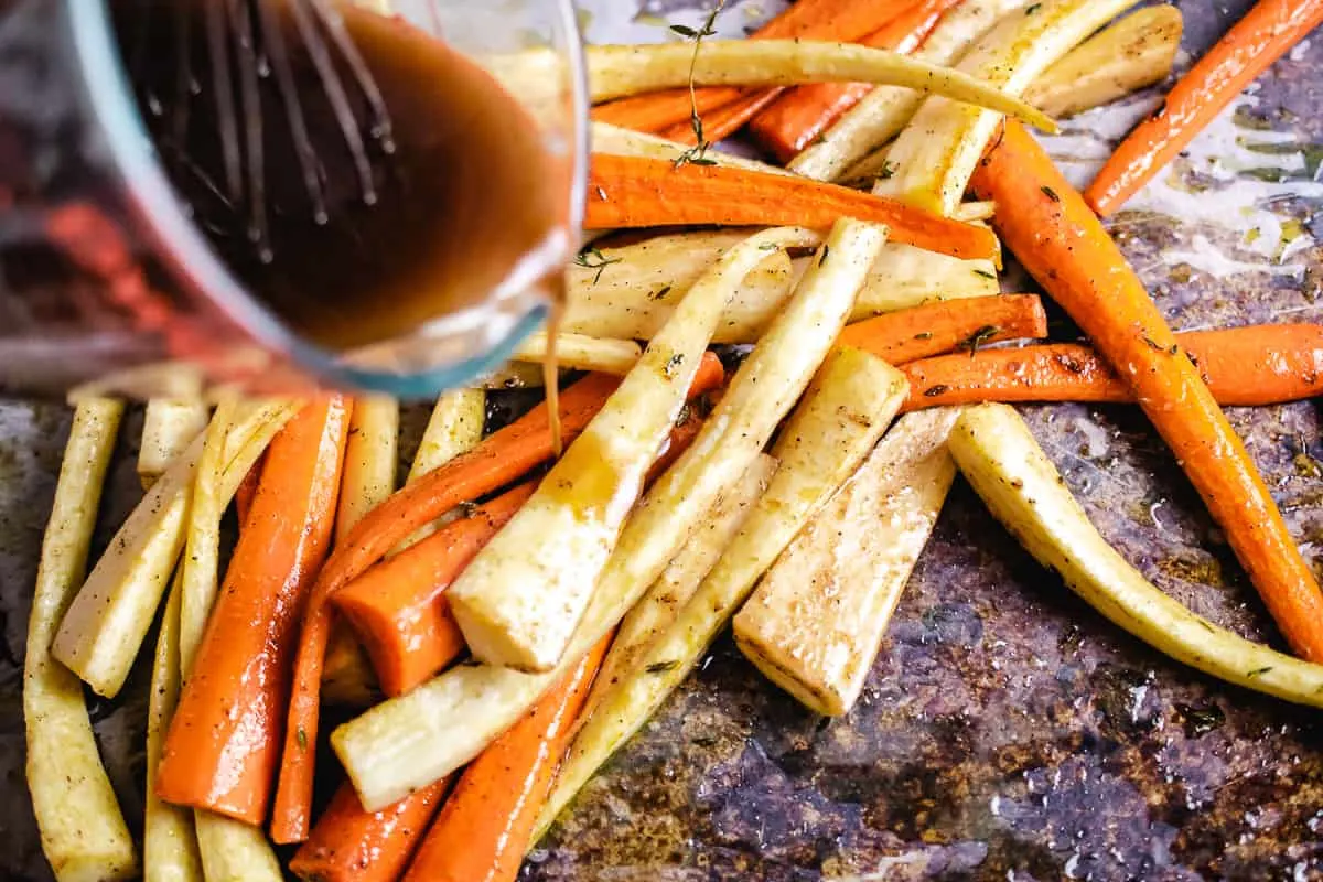 Melted butter, honey and balsamic vinegar glaze being poured onto carrots and parsnips.